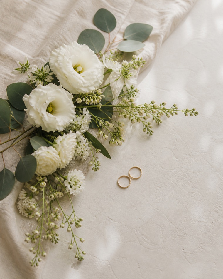 白い布の上に置かれた花と結婚指輪